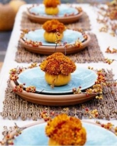 nell'imagine una tavola decorate con delle piccole zucche svuotate e riempite di fiori dal tipico colore arancio 