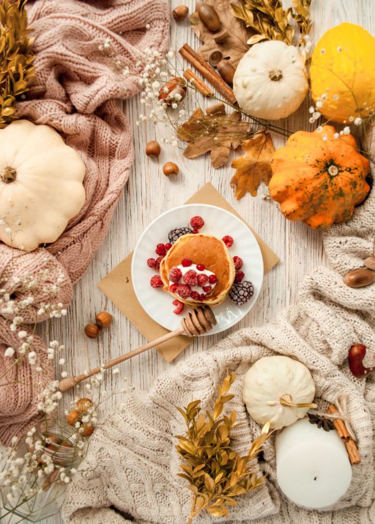 Una tavola di legno chiaro con tovaglie non convenzionale fatte di lana beige.  Protagoniste le  zucche, frutti di bosco, castagne, cannella e candele. la magia dell'autunno.