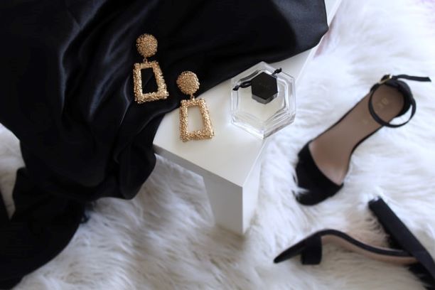 accessori moda sandalo alto nero orecchini dorati profumo su tessuto nero
